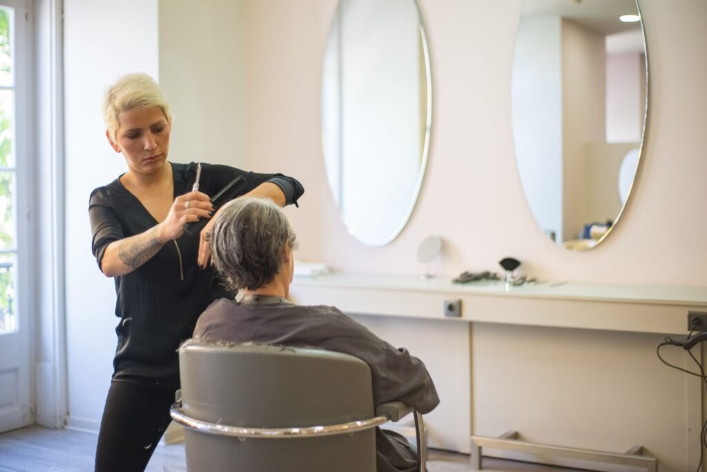 Cabeleireiro profissional sorrindo enquanto realiza um corte e atendimento personalizado em seu salão de beleza.